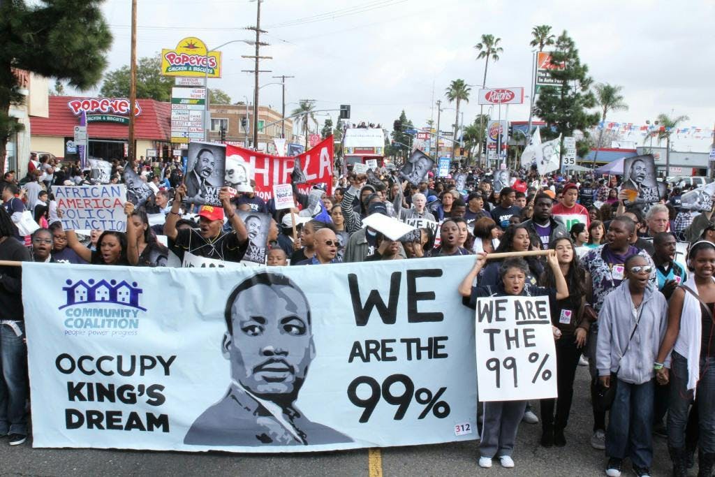 image of people leading a rally holding a sign from Community Coalition that says "Occupy King's Dream, We are the 99%"