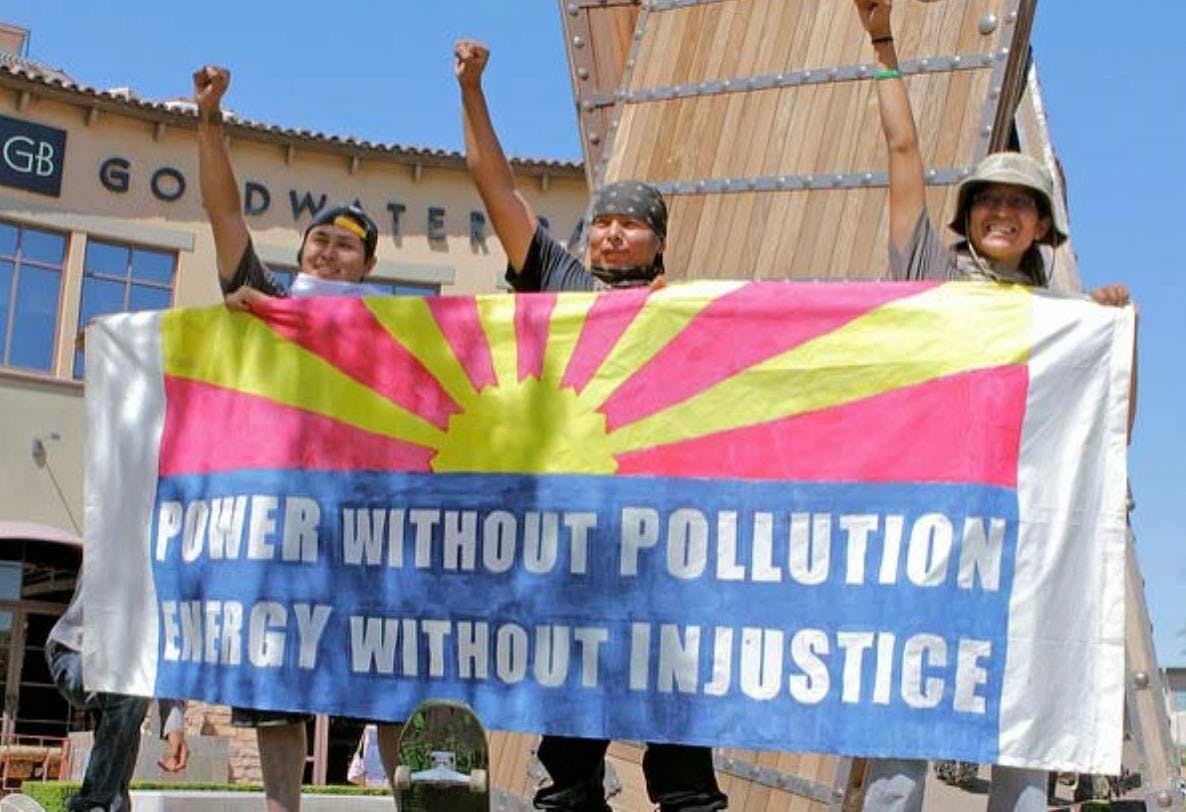 Three people holding a flag that says "power without pollution, energy without injustice"